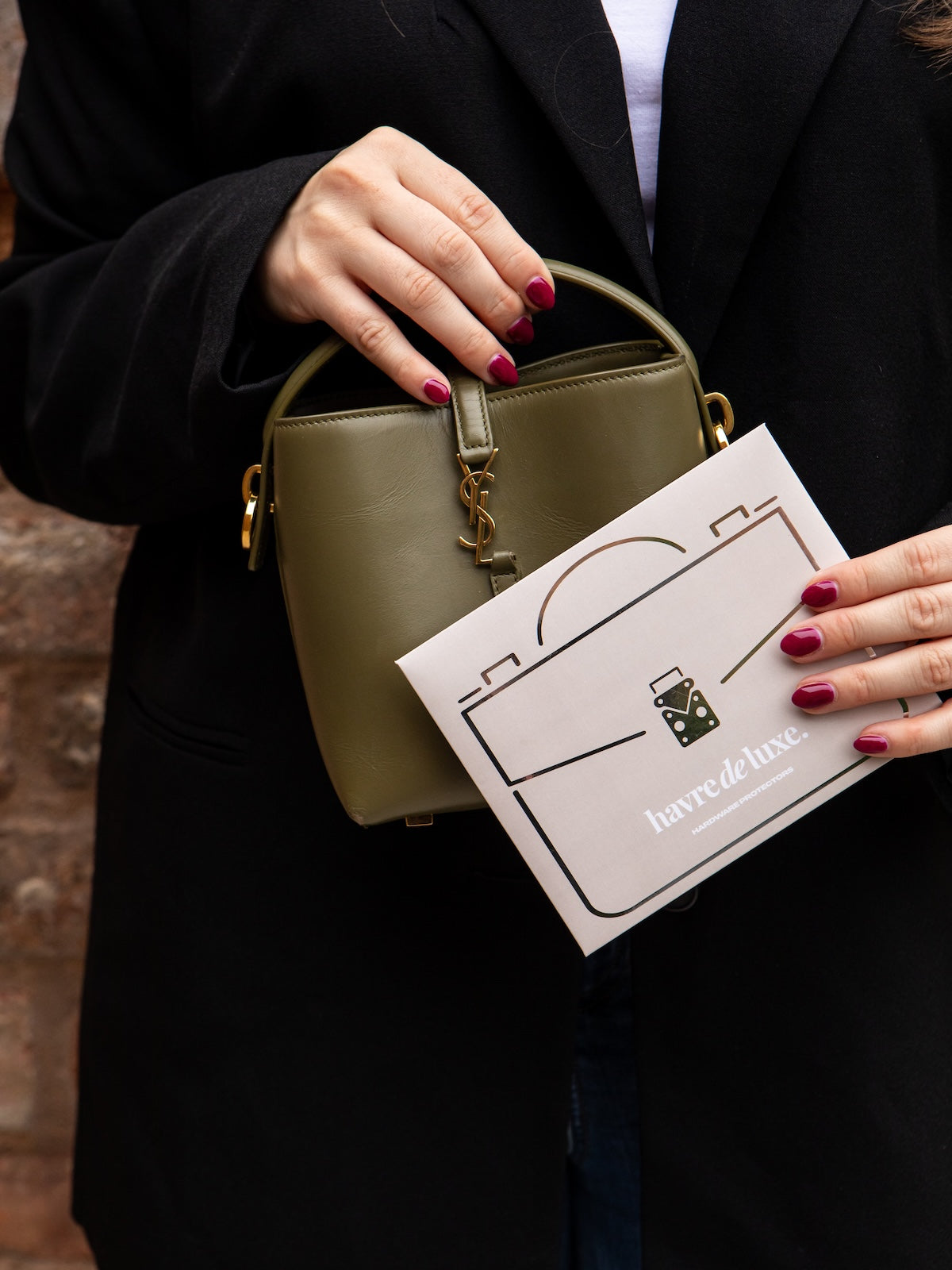 Person holding a green handbag and a card with a logo, wearing a dark coat.