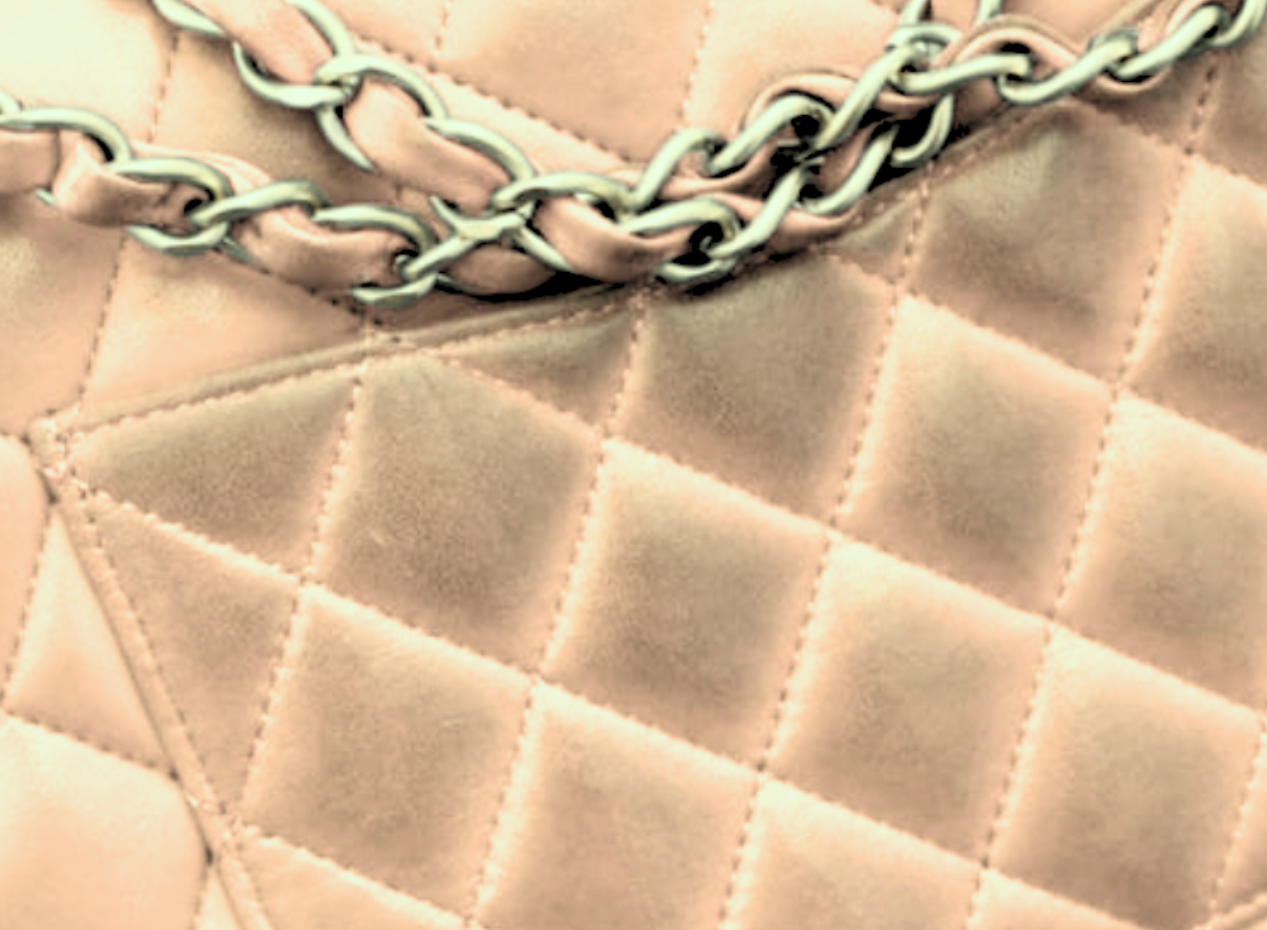 Close-up of a quilted light beige leather handbag with a silver chain strap gently resting on it